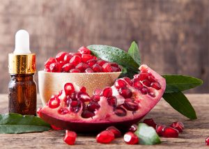 A bottle of pomegranate seed essential oil reverses sagging skin next to fresh pomegranite