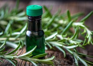 A bottle of rosemary essential oil next to fresh sprigs of rosemary