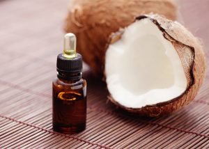 Bottle with dropper of coconut essential oil next to fresh coconuts