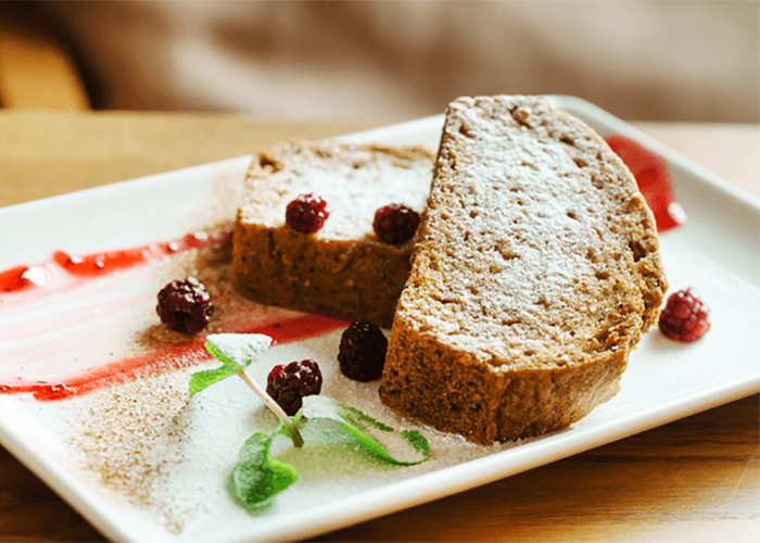 Slices of Keto carrot cake professionally displayed with icing sugar, cocoa, and raspberries