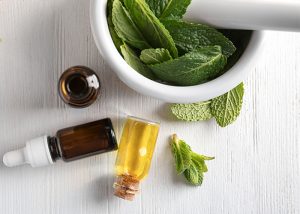 Top-down view of ginger and peppermint essential oil next to a mortar filled with fresh peppermint leaves.