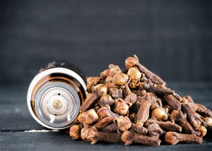 A bottle of ginger and clove essential oil blend next to a pile of cloves