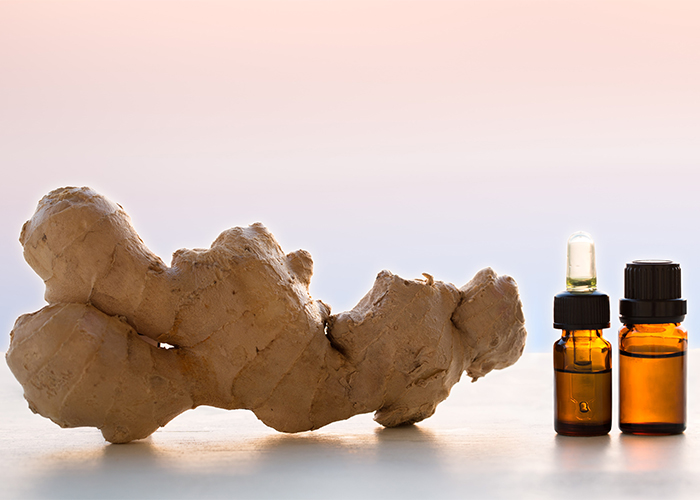Two bottles of ginger essential oil next to a whole ginger