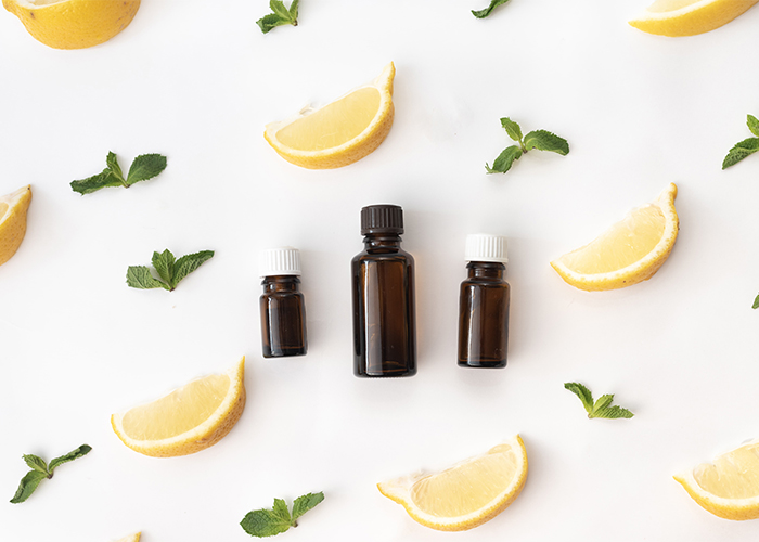 Bottles of Rise and Shine essential oil blend with lemon, peppermint, and frankincense oils surrounded by pieces of lemon wedges and mint leaves