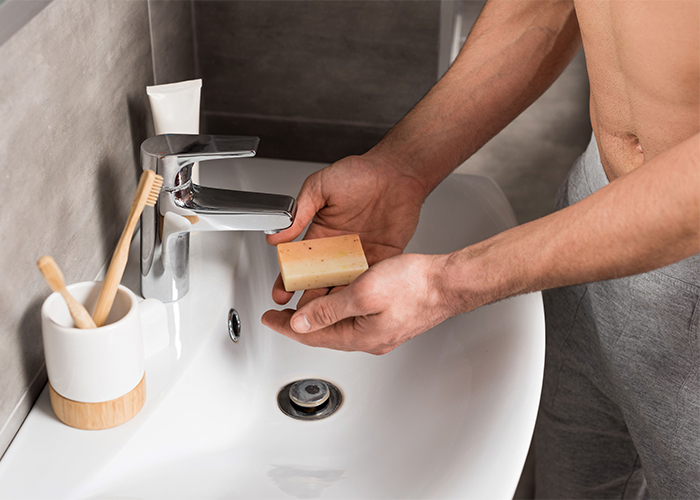Man at his sink holding a bar of handmade soap for men with essential oils