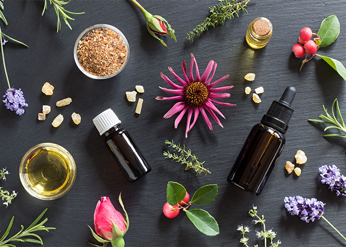 Flat lay of bottles of essential oils recipes for skin surrounded by a variety of fresh flowers
