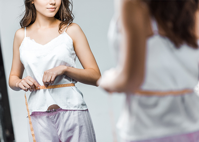 Slim woman on the Paleo diet using a measuring tape around her waist