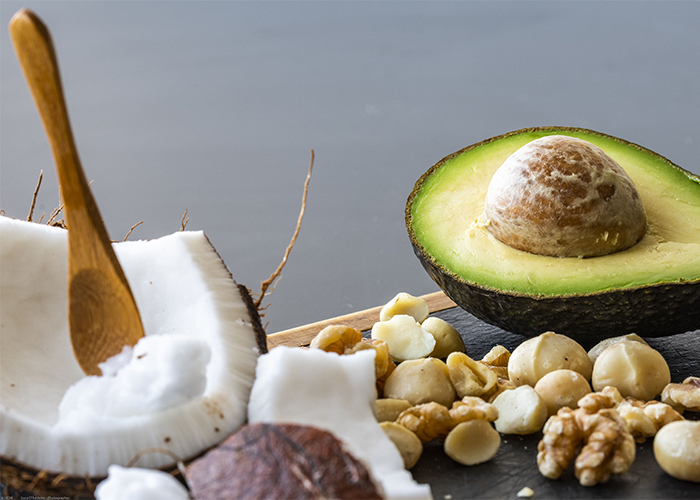 A halved coconut and avocado with mixed nuts scattered around