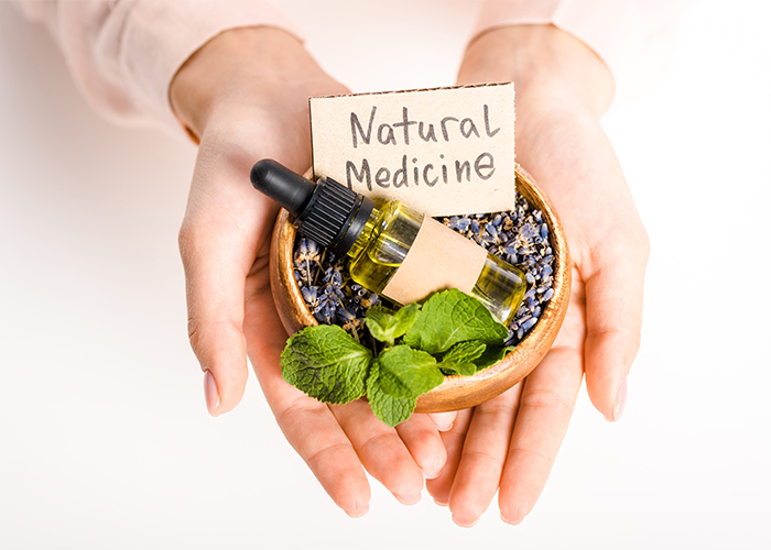 Woman holding a wooden bowl with a dropper bottle of essential oil filled with dried lavender and the sign "Natural Medicine"