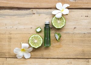 A top-down view of a clear bottle of bergamot essential oils beautifully arranged with a halved bergamot fruit and frangipani flowers 