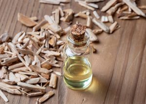 A bottle of sandalwood essential oil next to a pile of sandalwood pieces