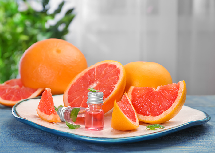 A plate with small bottles of grapefruit essential oil next to cut up pieces of pink grapefruit 