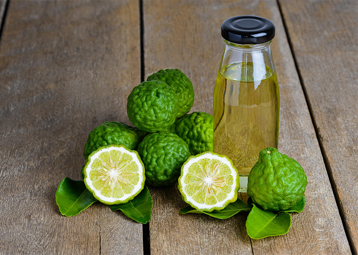 A pile of fresh bergamot fruits on a wooden table next to a bottle of homemade bergamot essential oil