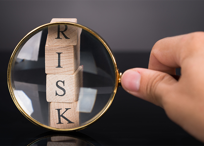 A woman using a magnifying glass to inspect wooden blocks that spell out "RISK"