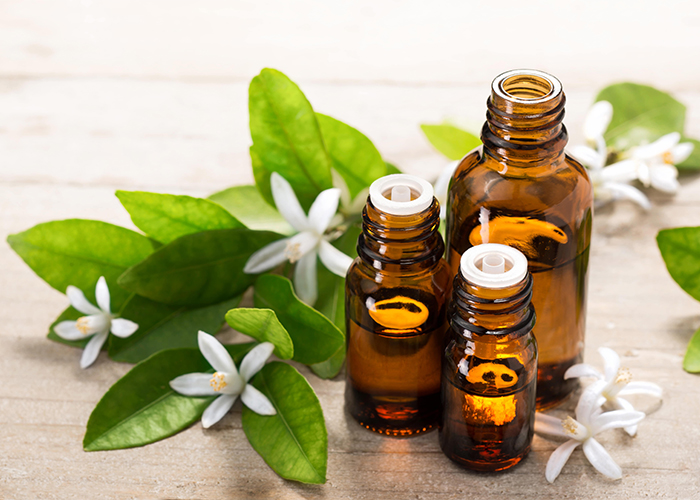 Different sized amber bottles filled with neroli essential oil next to neroli flowers and leaves