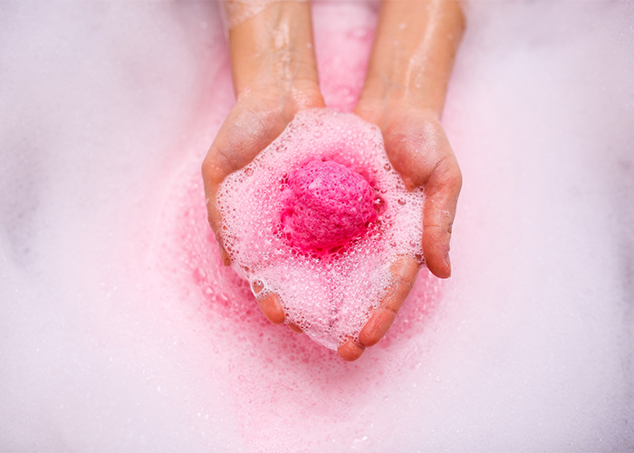 Woman holding a pink DIY manuka essential oil bath bomb with both hands in her bath