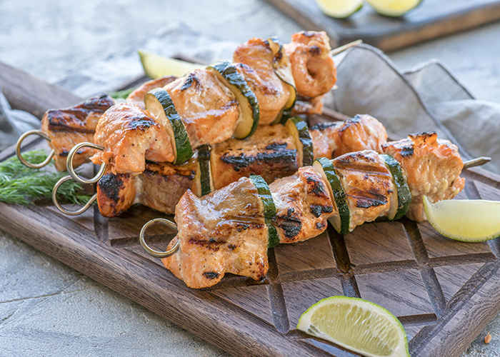 A wooden board with salmon and zucchini kebab skewers with slices of lime
