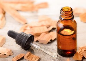 An open bottle of sandalwood essential oil with a dropper next to sandalwood pieces
