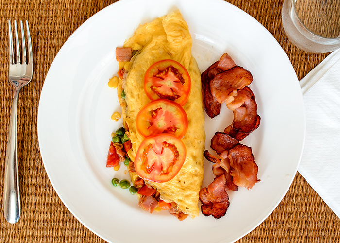 Keto burrito made with a stuffed omelette filled with chopped vegetables with a lashing of crispy bacon on the side