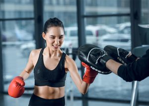 A woman in a boxing class punching the boxing pads her trainer is wearing 