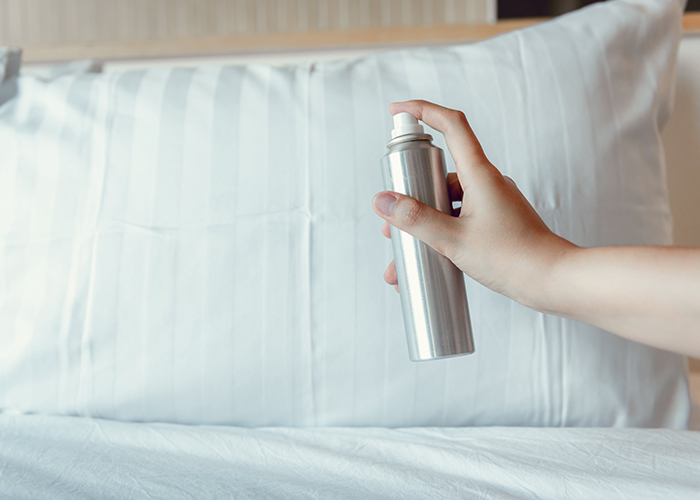 A woman spraying homemade essential oil mist in fun and floral aroma on her pillow and bed to help her sleep better
