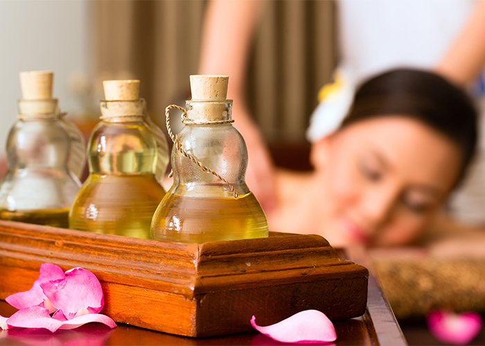 Bottles of essential oil blends for massage with a woman getting a massage in the background with them