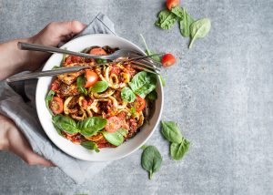 Top-down view of a woman holding a plate with chicken, noodles, and spinach leaves