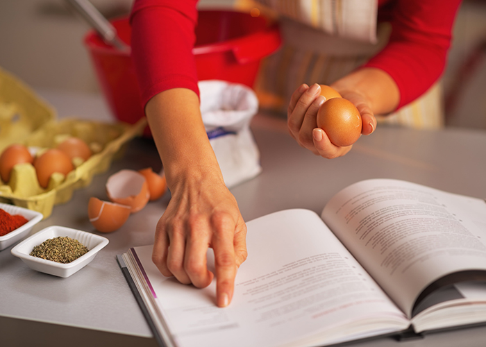 Woman reading a Paleo cookbook in her kitchen while holding eggs