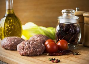 olive oil bottle with raw beef patties and chili peppers